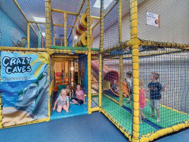 A play area with a netted structure and children playing at Tide’s Reach - Hayling Island