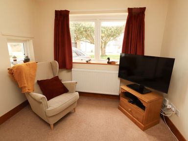 A living room with an armchair and a television at Sarah's Cottage