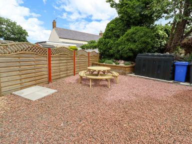 A garden with a table, benches, and bins at Sarah's Cottage
