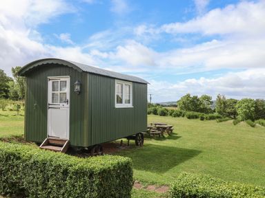 A shepherd's hut with a door and windows on a grassy area at Shepherds Hut at East Hill Pride Four Elms Hill Nr. Sidmouth