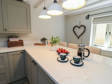A kitchen with a counter, coffee maker, cups, and strawberries at 2 The Gardens in Lechlade