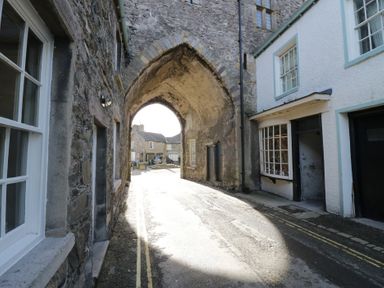 An arched doorway with stone walls and buildings on either side at Courtyard Cottage