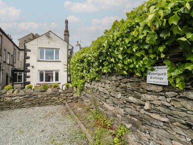 A house view with a stone wall and sign at Courtyard Cottage in Cartmel