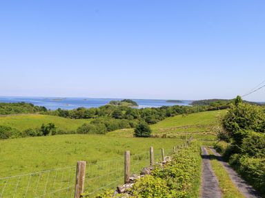 A view of a grassy landscape with a road and water at Mayfly Cottage
