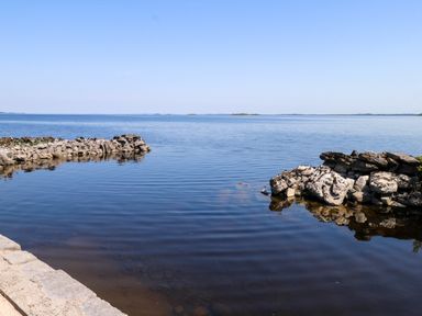A shoreline with rocks and water under a clear sky at Mayfly Cottage
