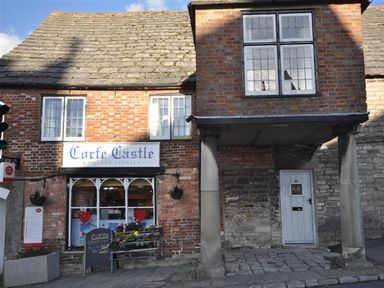 A storefront of Corfe Castle Village Stores with a sign and columns in Wareham