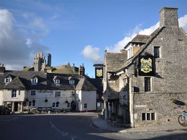 A pub and stone buildings in a street with a castle in the background at Little Wickers in Wareham