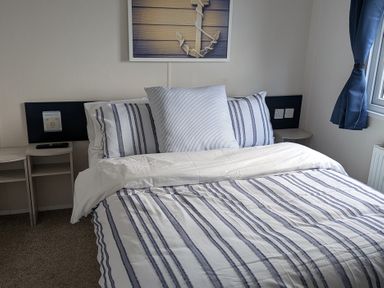 A bedroom with a bed and wall art at Presthaven - Denbigh Dunes Gronant