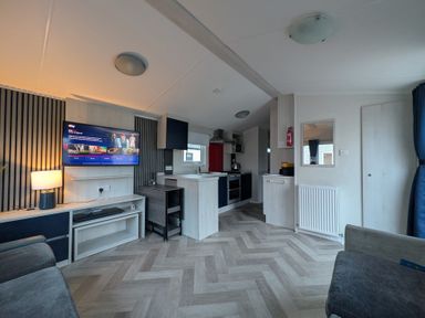 A living room with a tv and kitchen area at Presthaven - Denbigh Dunes in Gronant