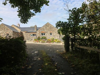 A stone house with a gravel driveway and gardens at The Old Dairy near Solva