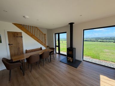 A dining room with a wood stove and large windows at High View Barn in Launceston