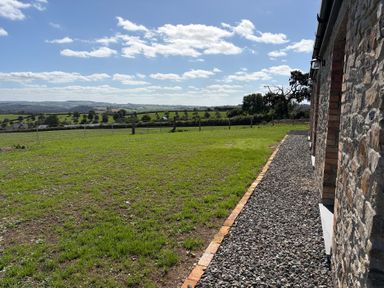 A grassy outdoor area with a gravel path and stone wall at High View Barn Launceston