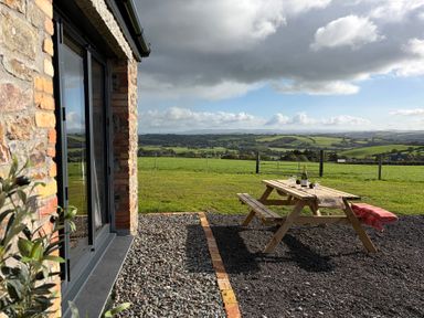 A picnic table with a bottle and glasses overlooking the landscape at High View Barn in Launceston