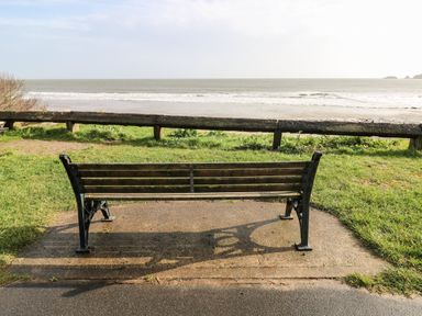 A bench facing the sea with a pathway at Coedrath Park 