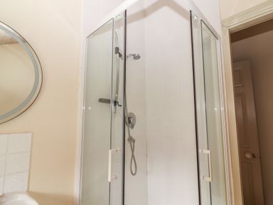 A shower enclosure with a mirror and tiles at The Coach House Cottage BALLYCOMMON