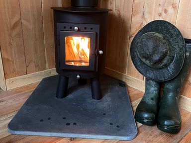 A wood stove with a fire, boots, and a hat at The Little Shepherds Hut with a View near Newbridge-On-Wye