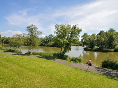 A person sitting near a river with trees and grass at Caravan in Dolton