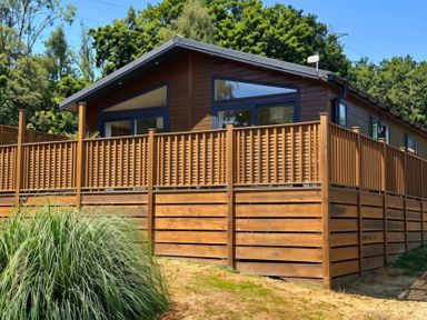 A cabin with a wooden deck surrounded by grass and trees at Lakeside Retreat in Newton Abbot