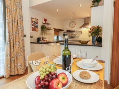 A kitchen with a dining table set and a bowl of fruits at Frome Gazey Barn in Frampton