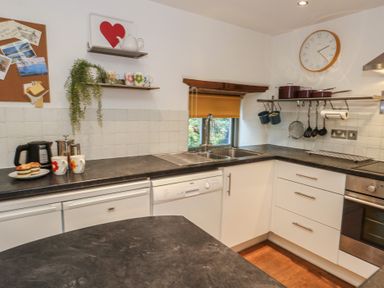 A kitchen with a sink, dishwasher, oven, and shelves at Frome Gazey Barn in Frampton