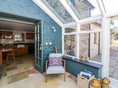 A conservatory with a chair and kitchen view at Yr Hen Felin Boncath