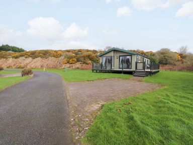 A house with decking and surrounding grass at 56 The Stables Pwllheli