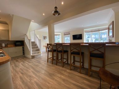 A kitchen with bar stools and staircase at Nesden House