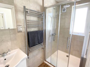 A bathroom with a shower, sink, towel rail, and towel at Nesden House