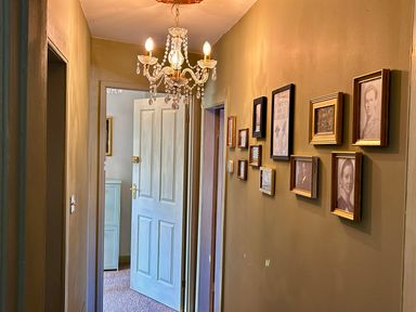 A hallway with a chandelier and framed photographs at Downton II in Alnwick
