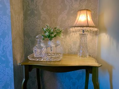 A table with a lamp, flower arrangement, decanter, and glasses at Downton II in Alnwick