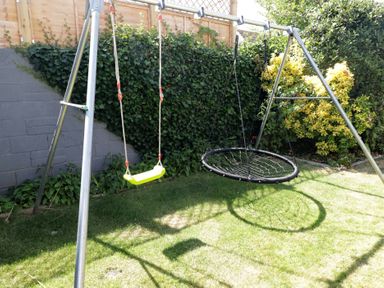 A swing set with a traditional swing and a nest swing in the garden at Ty Traeth in Porthcawl