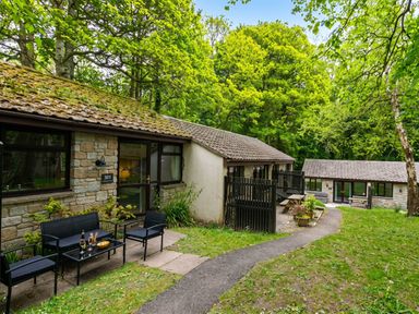 An outdoor view of a cabin with seating and trees at Painters Cottage 2Bed Chalet Free Leisure Passes Near St Ives