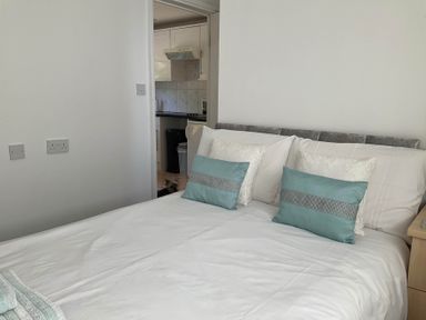 A bedroom with a bed and pillows visible towards a kitchen at Bungalow Sleeps 2 Parking in Newquay