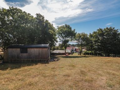 An outdoor area with a shed, trees, and houses in the distance at Owls Roost in Robin Hood’s Bay