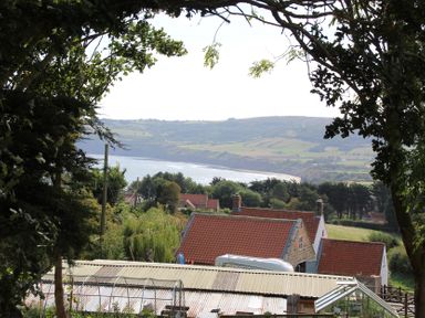 A view of the sea and hills with trees and houses at Owls Roost in Robin Hood’s Bay