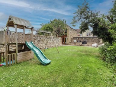 A garden with a playhouse, slide, and swing at Alma House in Seahouses