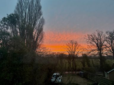 A sunset view with trees and a car at Fables Cottage in Otley, Suffolk