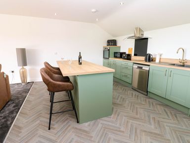 A kitchen with bar stools and appliances at Silver Birch Cottage in Frizington