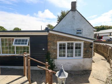 The exterior of a house with a stone wall and windows at Greenwich Cottage in Burton Bradstock