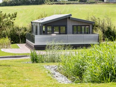 A house with patio and surrounding grass at Hideaway Lodge Llanfechell