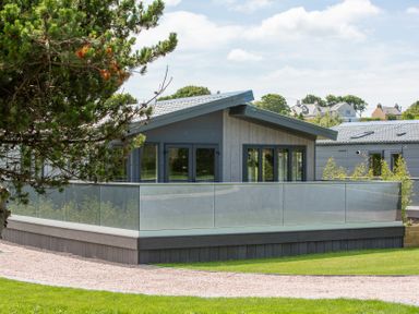 A house with a deck and glass railing at Hideaway Lodge Llanfechell