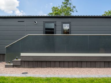 An exterior view of a building with a deck and glass railing at Hideaway Lodge Llanfechell