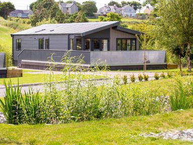 A house with a deck and surrounding grass at Hideaway Lodge in Llanfechell