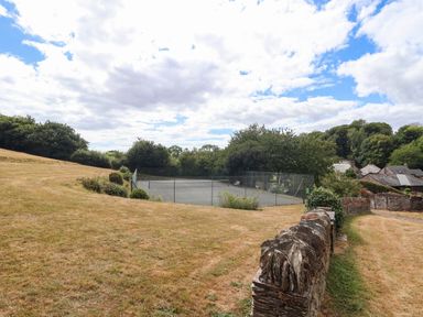 A tennis court surrounded by grass and trees at Iris at Stancombe Manor Sherford near Chillington
