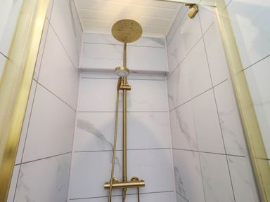 A shower with a gold showerhead and valve at Hedley Dene Cottage Longhorsley