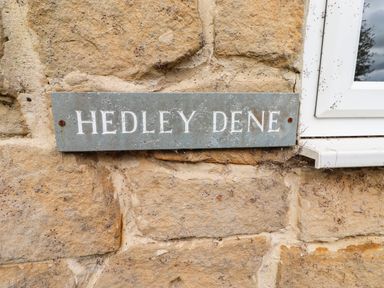 A sign displaying 'HEDLEY DENE' attached to a stone wall at Hedley Dene Cottage in Longhorsley