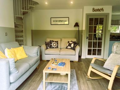 A living room with a sofa, armchair, coffee table, and spiral staircase at 2 Bedrooms overlooking Little Petherick Creek in Little Petherick