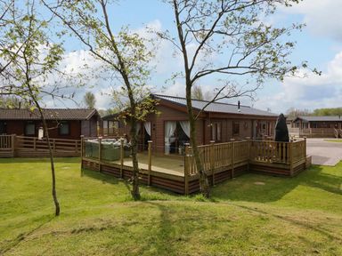 A lodge with a deck and trees at Lakeland Lodge 3Bed 2 Bath Private Patio in Carnforth