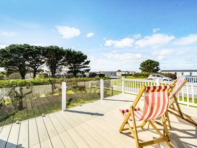 A view of deck chairs on a wooden deck with trees and a blue sky at 2Br Lodge Pool Fireplace PetsOK Parking in Goonhavern