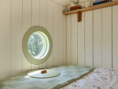 A bedroom with a round window and a bed at Cosy Luxury Owls Roost Hut with Private Hot Tub near Little Deptford Farm near Umberleigh
